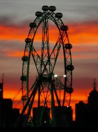 Low angle view of silhouette ferris wheel against dramatic sky