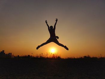 Silhouette person with arms raised jumping against clear sky during sunset