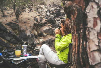 Woman sitting on rock by tree trunk