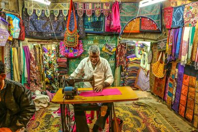 Mature tailor sewing textile on machine in store