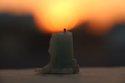 Close-up of wax candle against orange sky during sunset