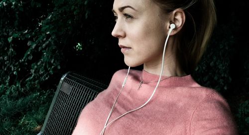 Close-up of thoughtful woman listening to music through in-ear headphones