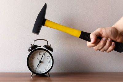 Close-up of hand holding clock on table against wall