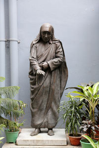 Statue of woman standing by potted plant against wall