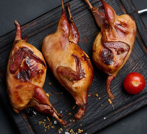 Frying carcasses of quails lie on a wooden board with vegetables, a black table