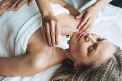 Young blonde woman enjoys facial massage with microcurrent facial massager 