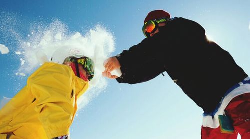 Low angle view of two people having snow ball fight against blue sky