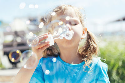 Girl blowing bubbles through wand on sunny day