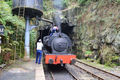 Rear view of men filling water in steam train