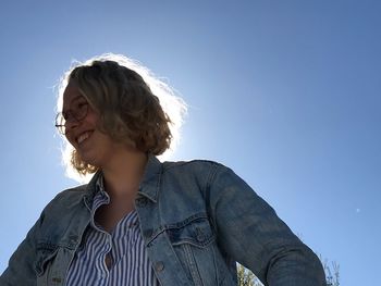 Low angle view of smiling young woman against clear sky
