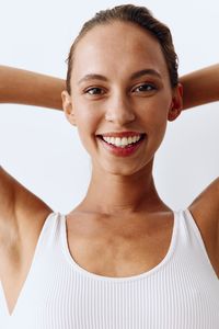 Close-up of young woman with arms raised standing against white background