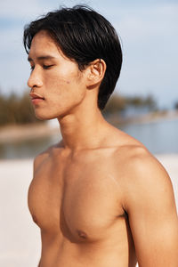 Close-up of shirtless young woman standing at beach