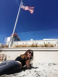Portrait of woman lying at beach with american flag in background against clear blue sky