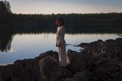 Woman standing on rock by lake during sunset