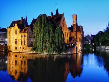 Buildings by river against clear blue sky at dusk