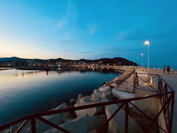 Illuminated city by sea against sky at dusk