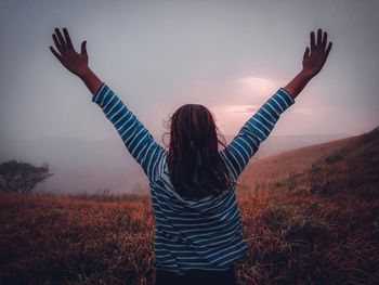 Rear view of woman with arms raised standing on land against sky