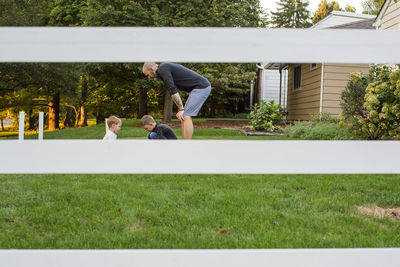 View through a fence of a father playing with children in yard