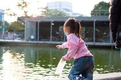The little girl is feeding fish in the park pond.