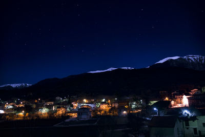 Illuminated town by mountains against sky at night