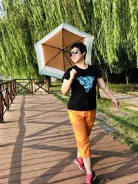 Woman with umbrella wearing sunglasses while walking on footpath