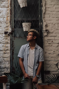 Young man looking away against brick wall