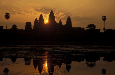 Silhouette temple reflecting in pond against sky during sunset