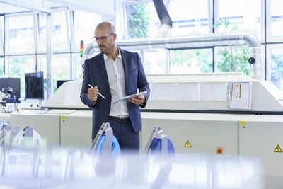 Mature male professional holding digital tablet while looking at machinery in factory