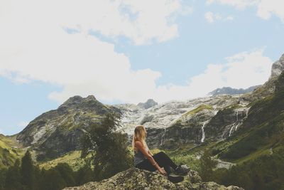 Side view of female hiker relaxing on rock at mountains against sky