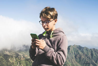 Full length of boy using mobile phone against sky