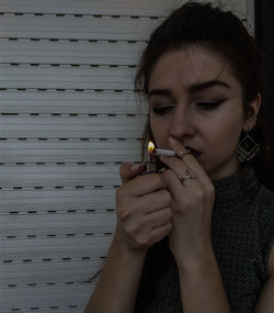 Close-up of young woman lighting cigarette against wall