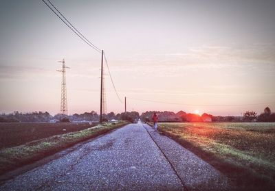 Road passing through field at sunset