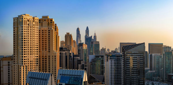 Modern buildings in city against sky during sunset