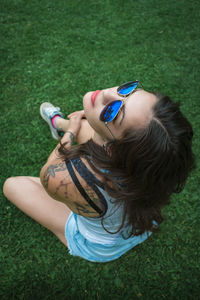 High angle view of beautiful woman wearing sunglasses while sitting on grassy field