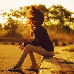 Side view of woman tossing hair while sitting on footpath