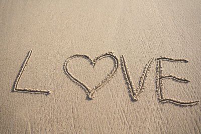 The word love written in the sand on the beach with heart sign and copy space. love is all you need