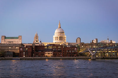 Church amidst city by river against clear sky