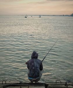 Rear view of man fishing in sea against sky