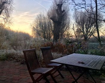 Chairs and table by trees against sky during sunset