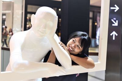 Smiling young woman standing by statue in shopping mall