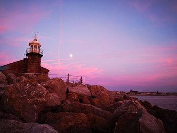 Lighthouse on rock by sea against sky during sunset