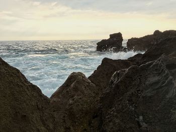 Rock formation on beach against sky during sunset