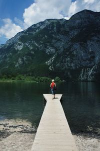 Rear view of woman standing on pier at lake against sky