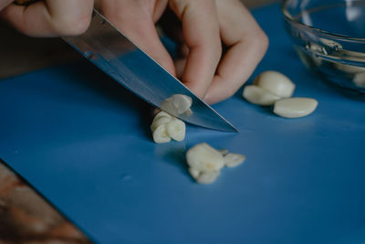 Cuts garlic on a blue plate, with a kitchen knife, close-up, cooking homemade food