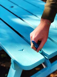 Cropped hand of man painting wooden bench