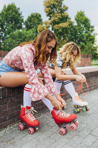 Smiling woman with friend tying lace of roller skates