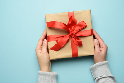 Cropped hand of woman holding gift box over blue background