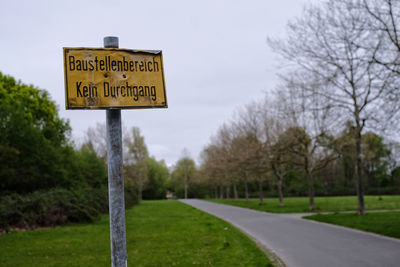 Information sign on road by trees against sky