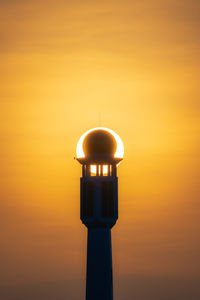 Low angle view of illuminated lighthouse against orange sky