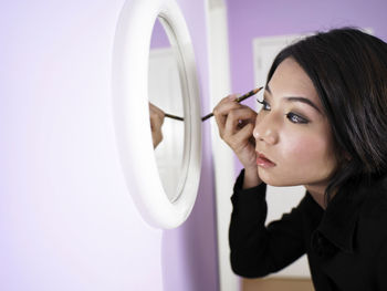 Woman applying eyeliner while looking in mirror at home